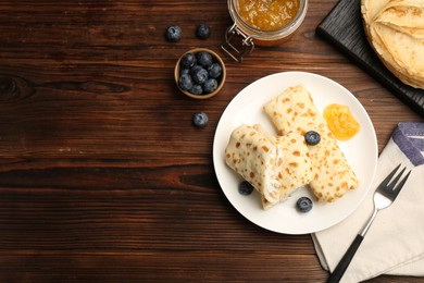 Photo of Delicious crepes with cottage cheese, jam and blueberries served on wooden table, flat lay. Space for text