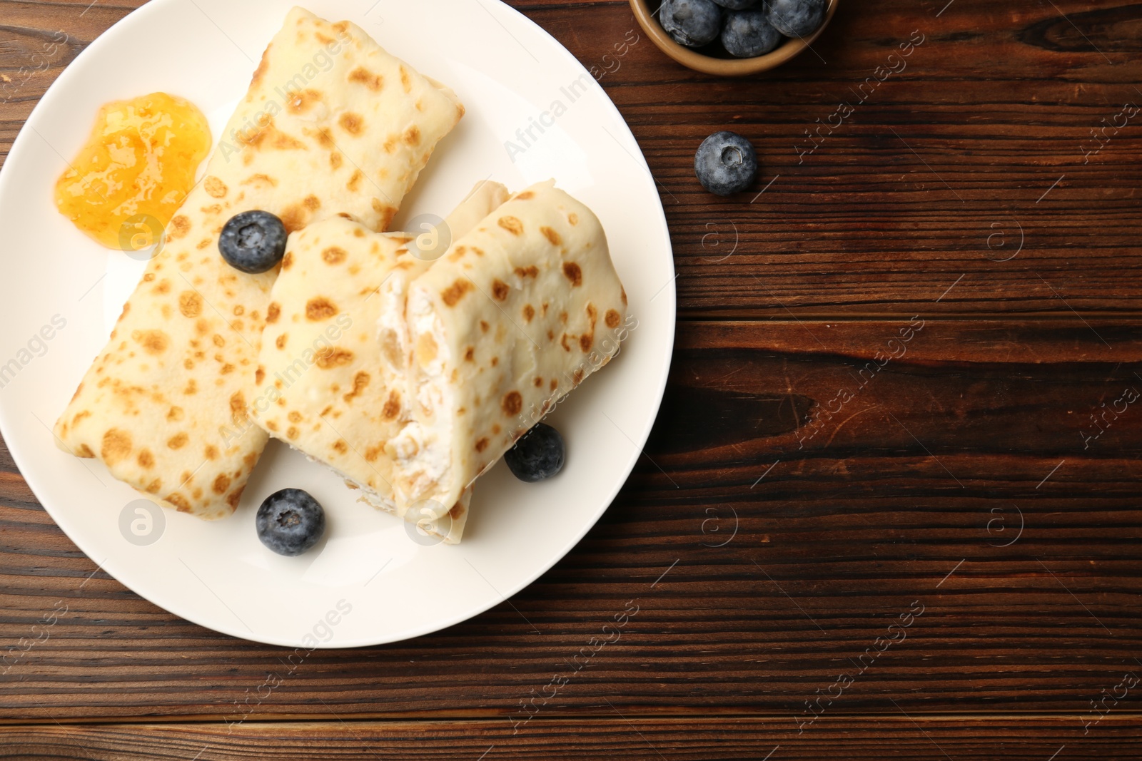 Photo of Delicious crepes with cottage cheese, jam and blueberries on wooden table, top view. Space for text