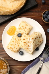 Photo of Delicious crepes with cottage cheese, jam and blueberries served on wooden table, flat lay