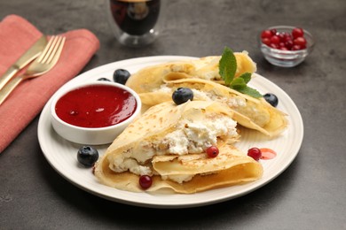 Photo of Delicious crepes with cottage cheese, jam, redcurrants and blueberries served on grey table, closeup