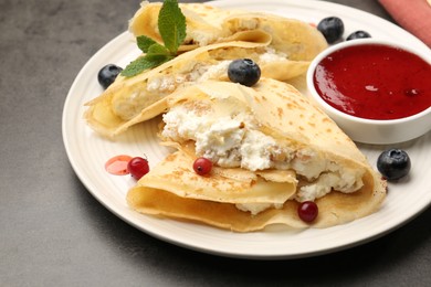 Photo of Delicious crepes with cottage cheese, jam, redcurrants and blueberries on grey table, closeup