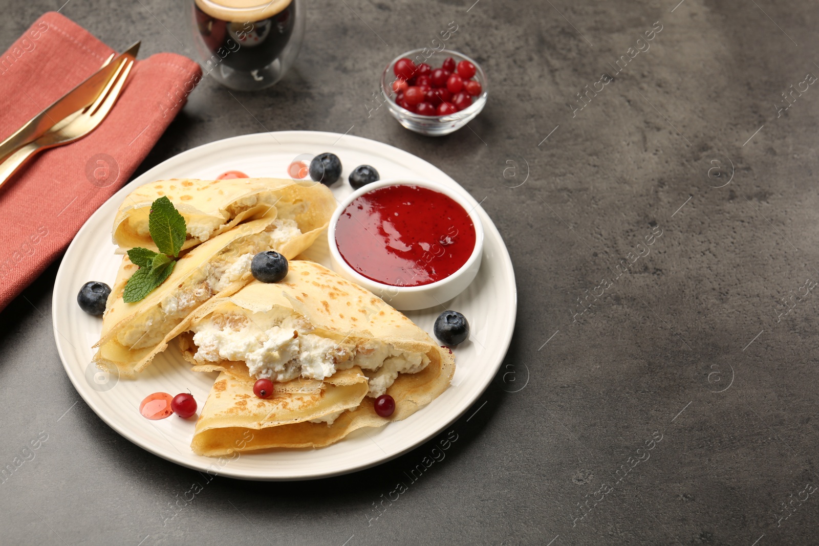 Photo of Delicious crepes with cottage cheese, jam, redcurrants and blueberries served on grey table. Space for text