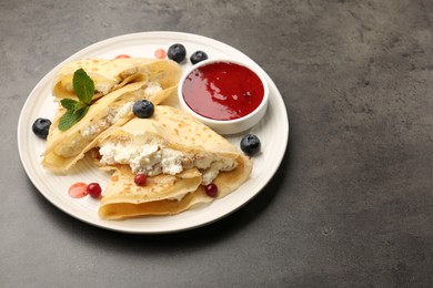 Photo of Delicious crepes with cottage cheese, jam, redcurrants and blueberries on grey table