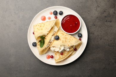 Photo of Delicious crepes with cottage cheese, jam, redcurrants and blueberries on grey table, top view