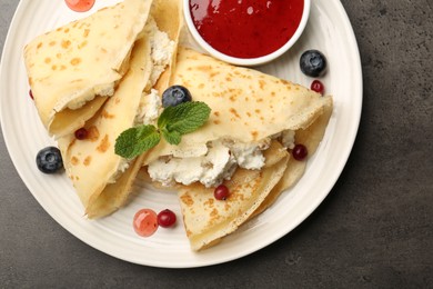 Photo of Delicious crepes with cottage cheese, jam, redcurrants and blueberries on grey table, top view