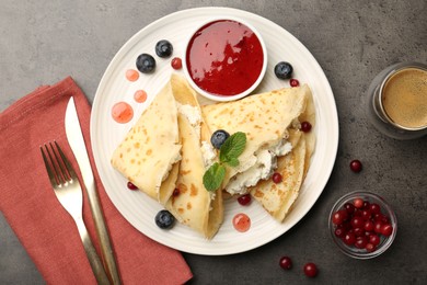 Photo of Delicious crepes with cottage cheese, jam, redcurrants and blueberries served on grey table, flat lay