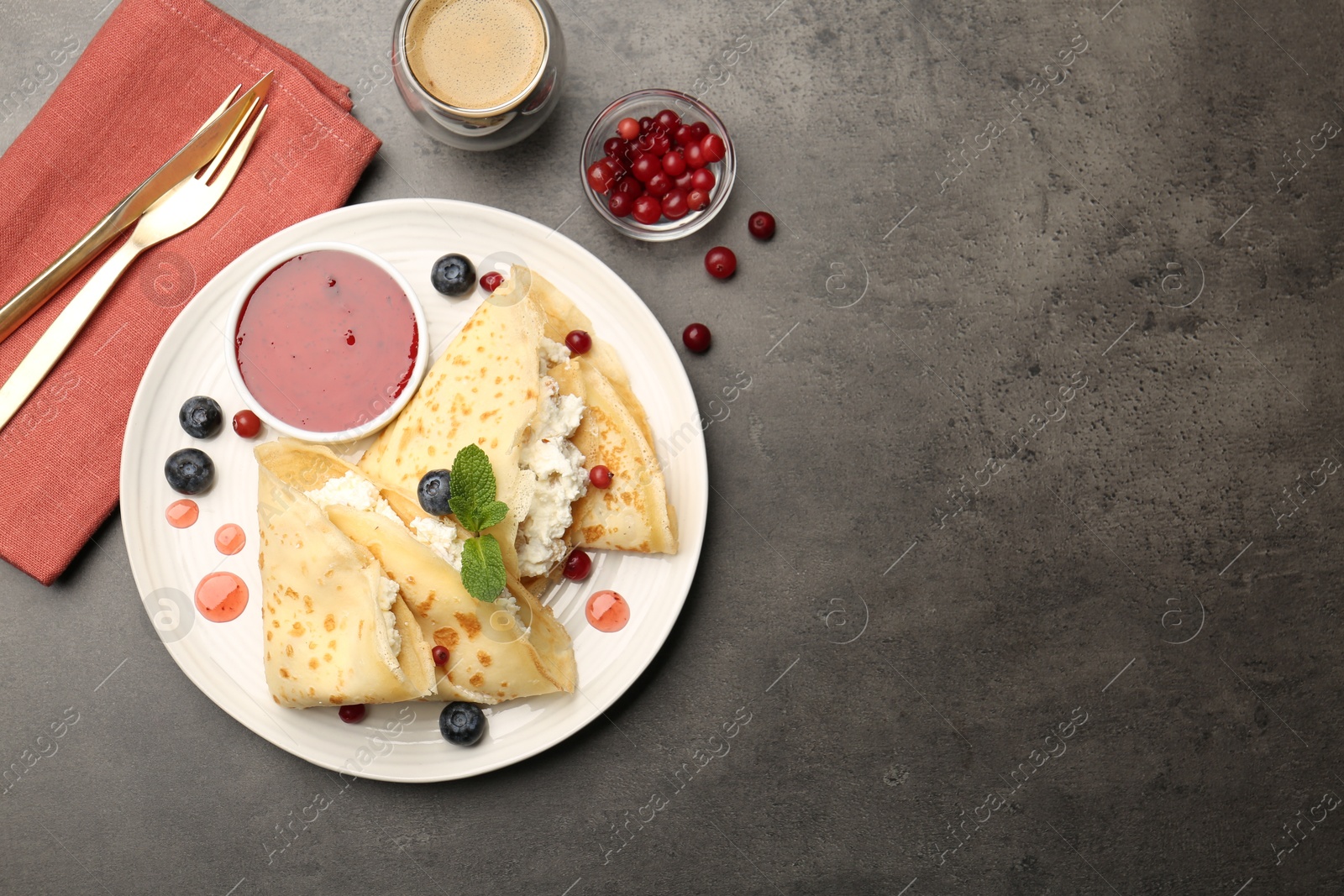 Photo of Delicious crepes with cottage cheese, jam, redcurrants and blueberries served on grey table, flat lay. Space for text