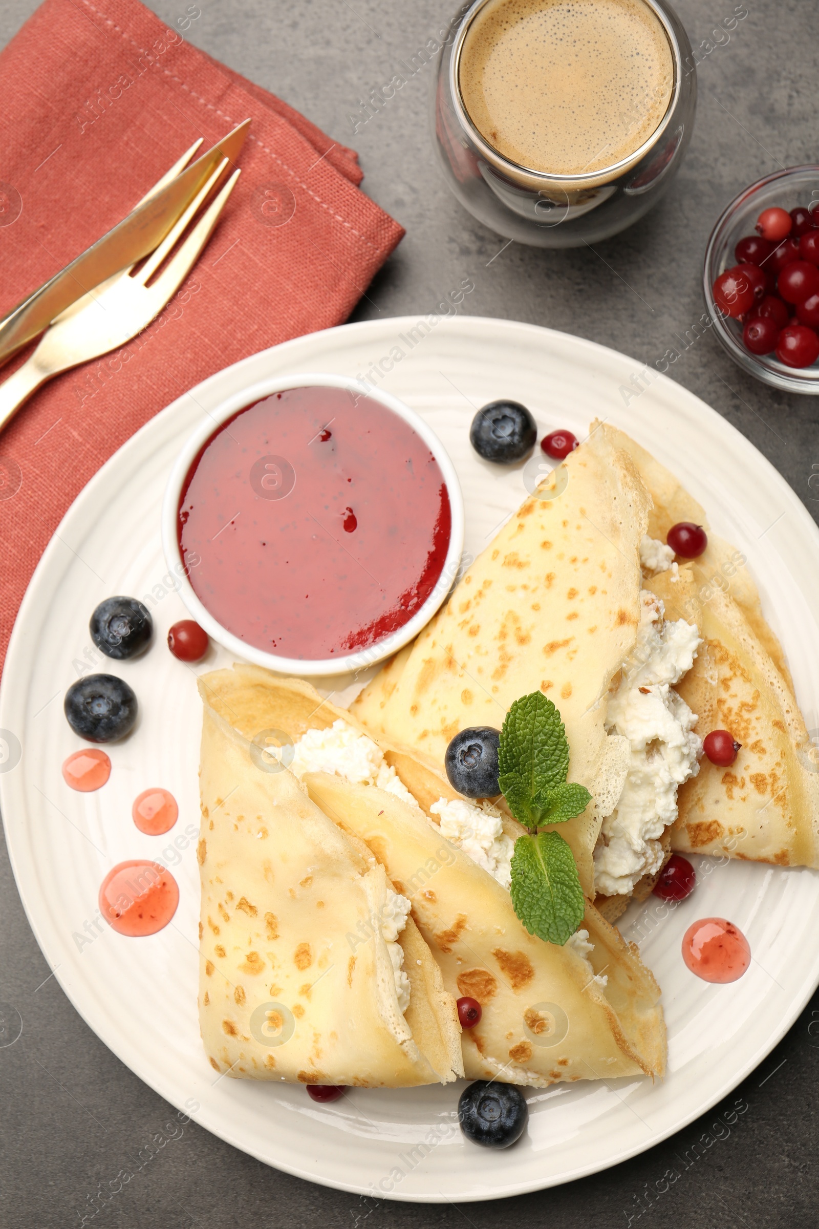 Photo of Delicious crepes with cottage cheese, jam, redcurrants and blueberries served on grey table, flat lay