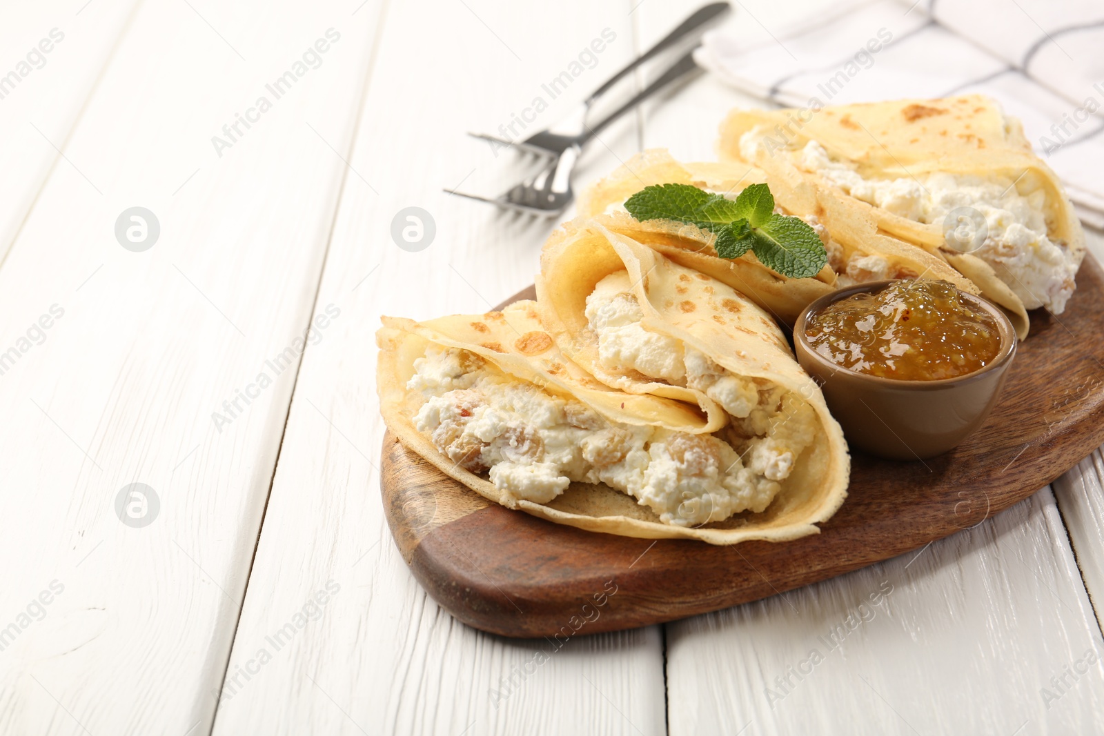 Photo of Delicious crepes with cottage cheese, jam and mint on white wooden table, closeup. Space for text