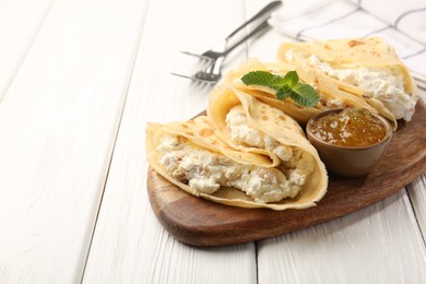 Photo of Delicious crepes with cottage cheese, jam and mint on white wooden table, closeup. Space for text