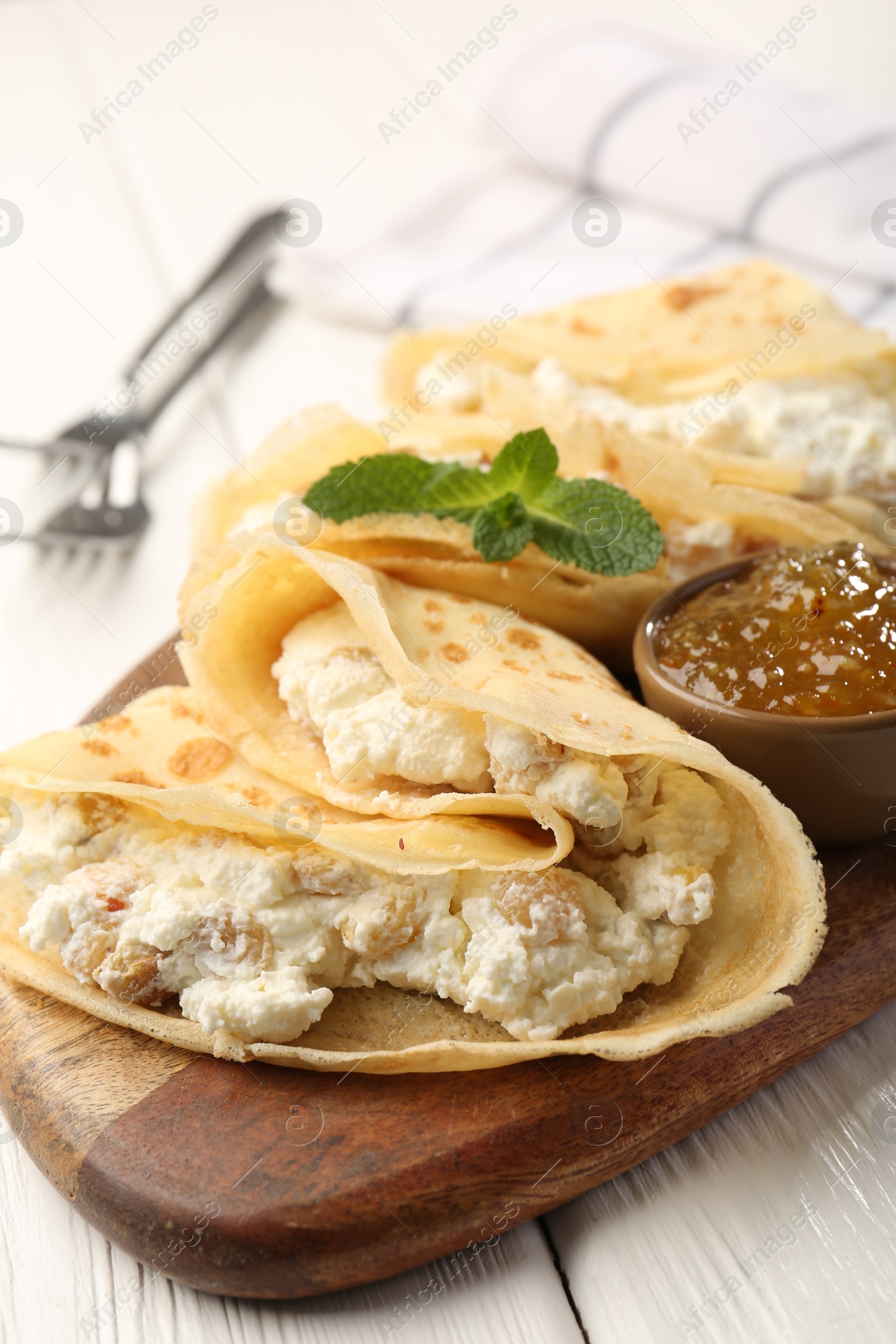 Photo of Delicious crepes with cottage cheese, jam and mint on white wooden table, closeup