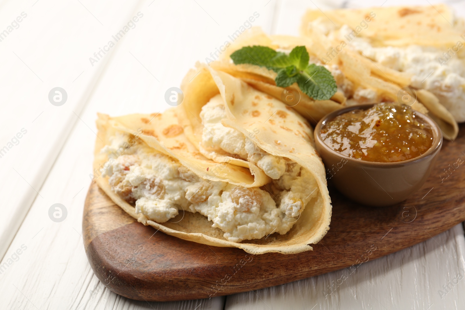 Photo of Delicious crepes with cottage cheese, jam and mint on white wooden table, closeup