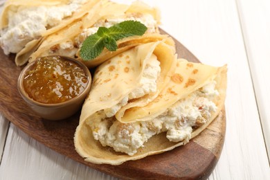 Photo of Delicious crepes with cottage cheese, jam and mint on white wooden table, closeup