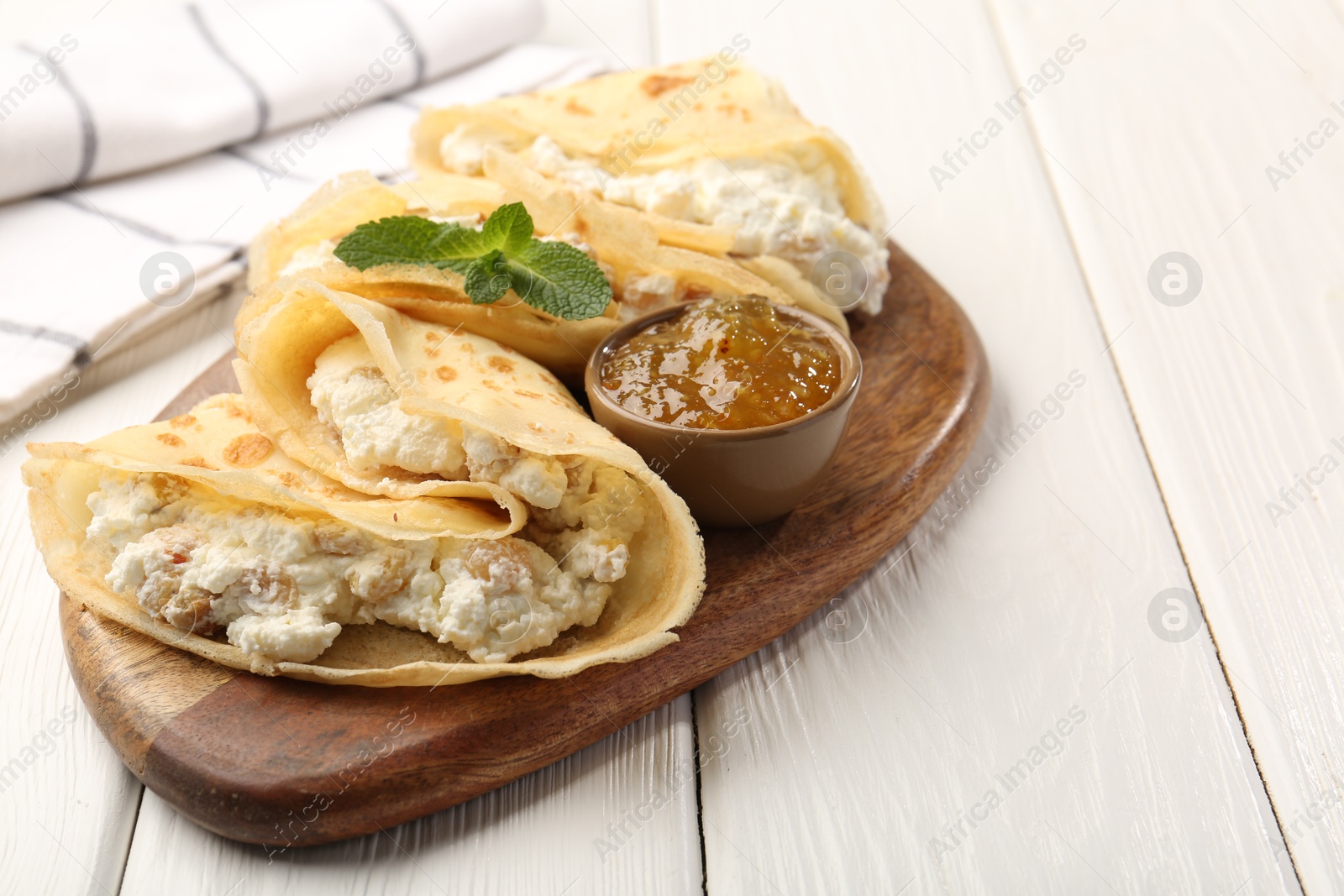 Photo of Delicious crepes with cottage cheese, jam and mint on white wooden table, closeup