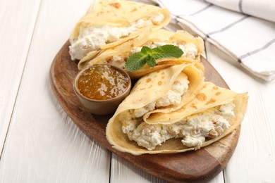 Photo of Delicious crepes with cottage cheese, jam and mint on white wooden table, closeup