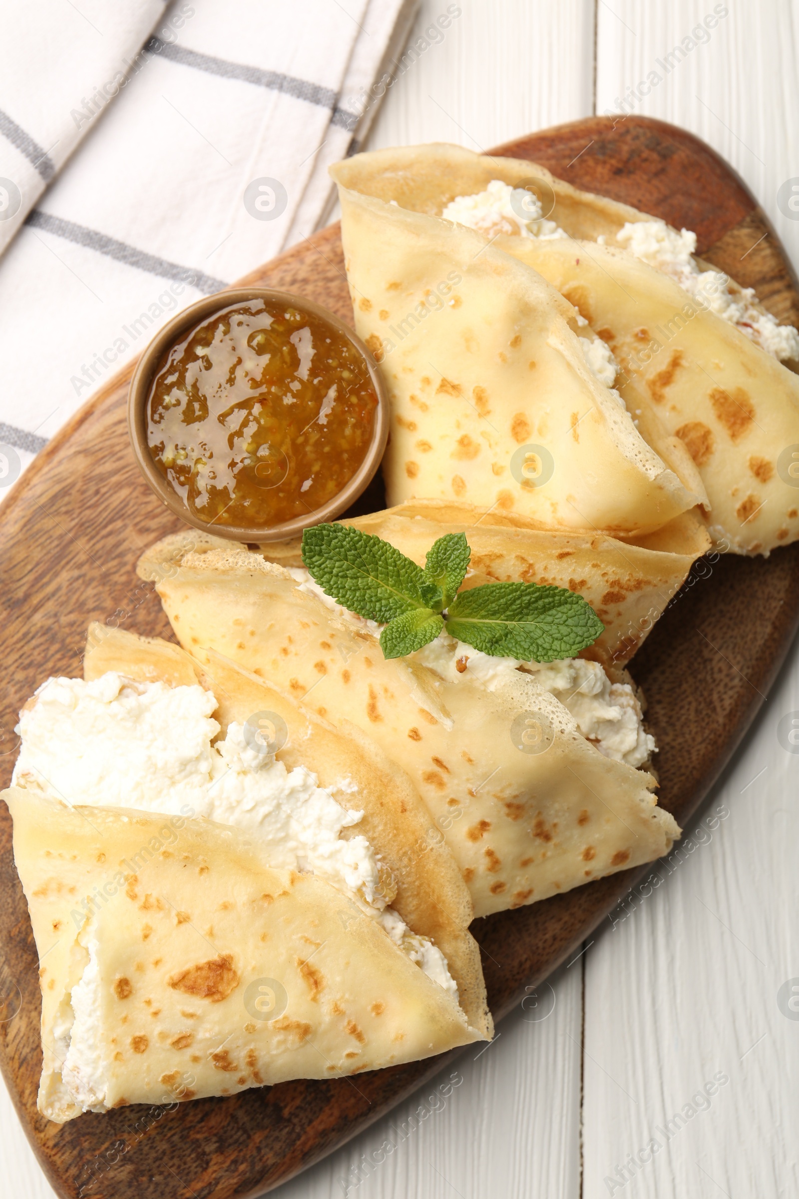 Photo of Delicious crepes with cottage cheese, jam and mint on white wooden table, top view