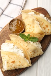 Photo of Delicious crepes with cottage cheese, jam and mint on white wooden table, top view