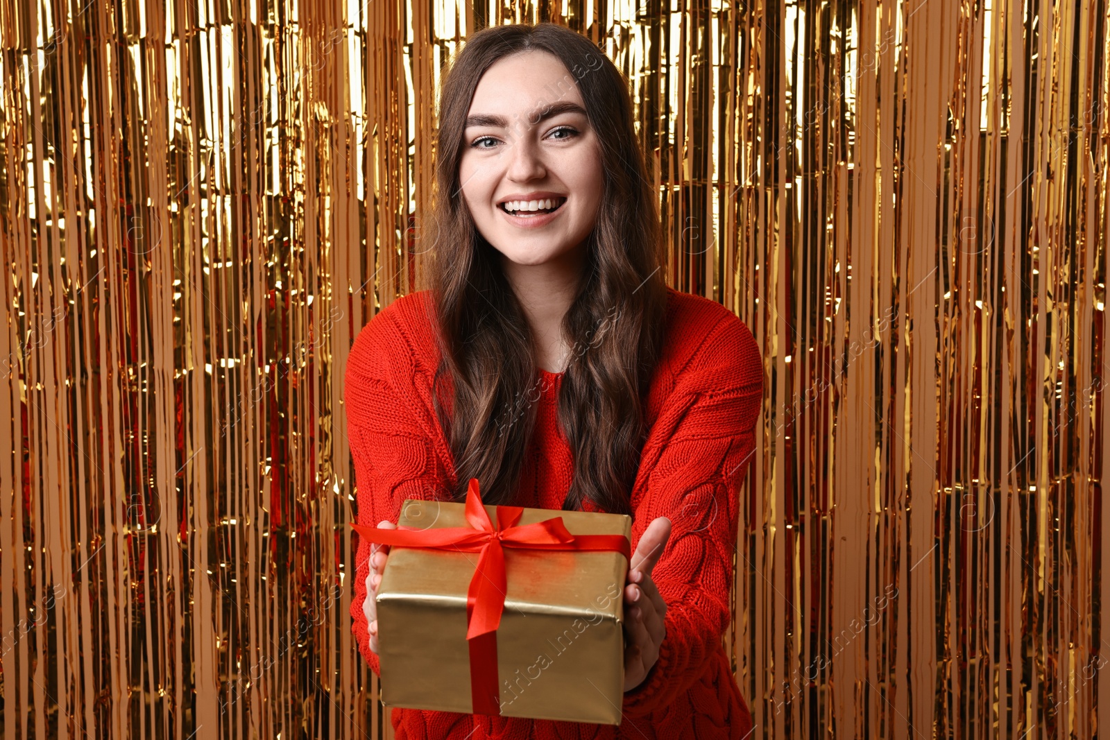 Photo of Happy young woman with gift box against golden foil curtain