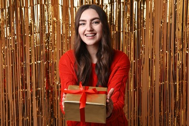 Photo of Happy young woman with gift box against golden foil curtain