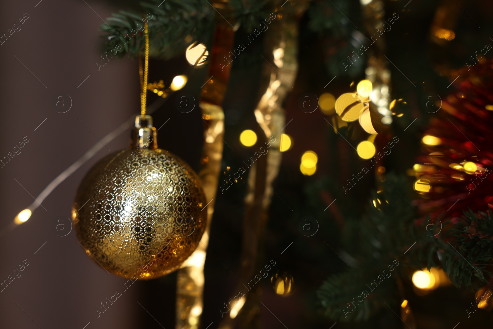 Photo of Shiny tinsels and bauble on Christmas tree against blurred lights, closeup