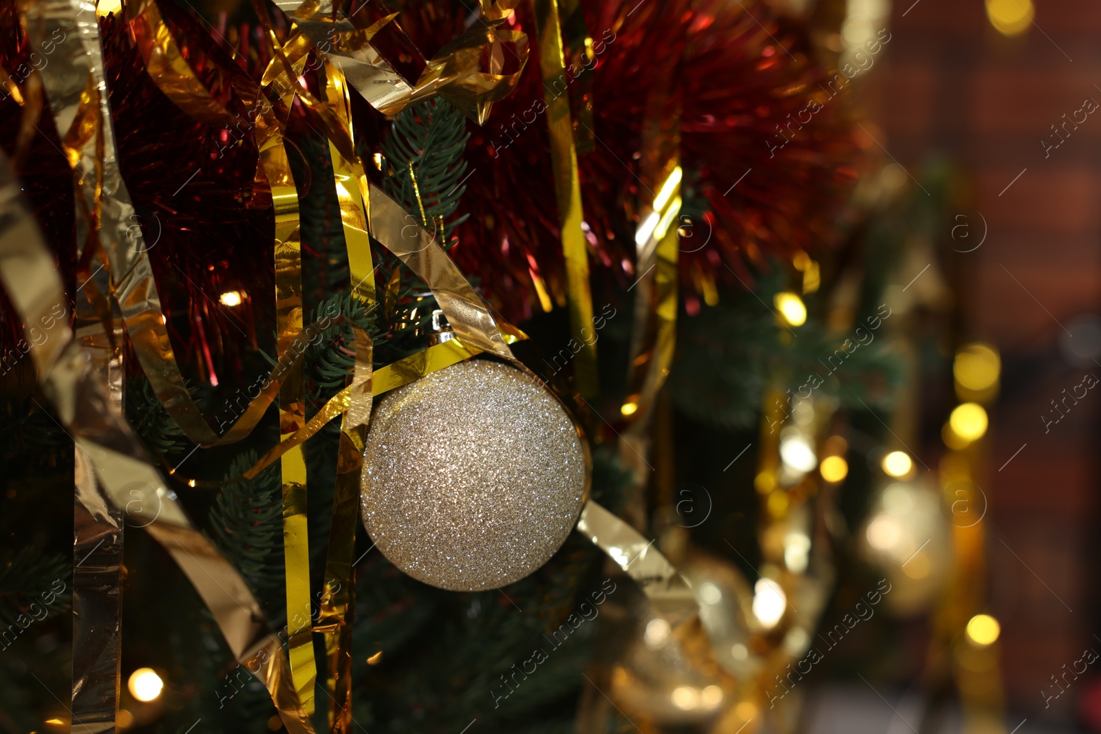 Photo of Shiny tinsels and bauble on Christmas tree against blurred lights, closeup