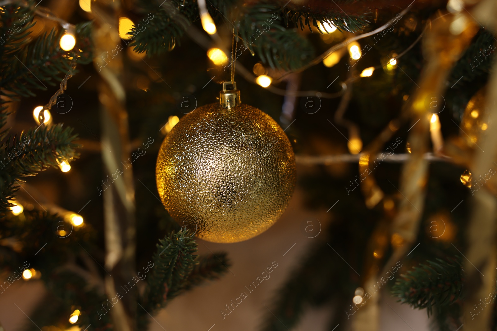 Photo of Shiny tinsels, bauble and festive lights on Christmas tree, closeup