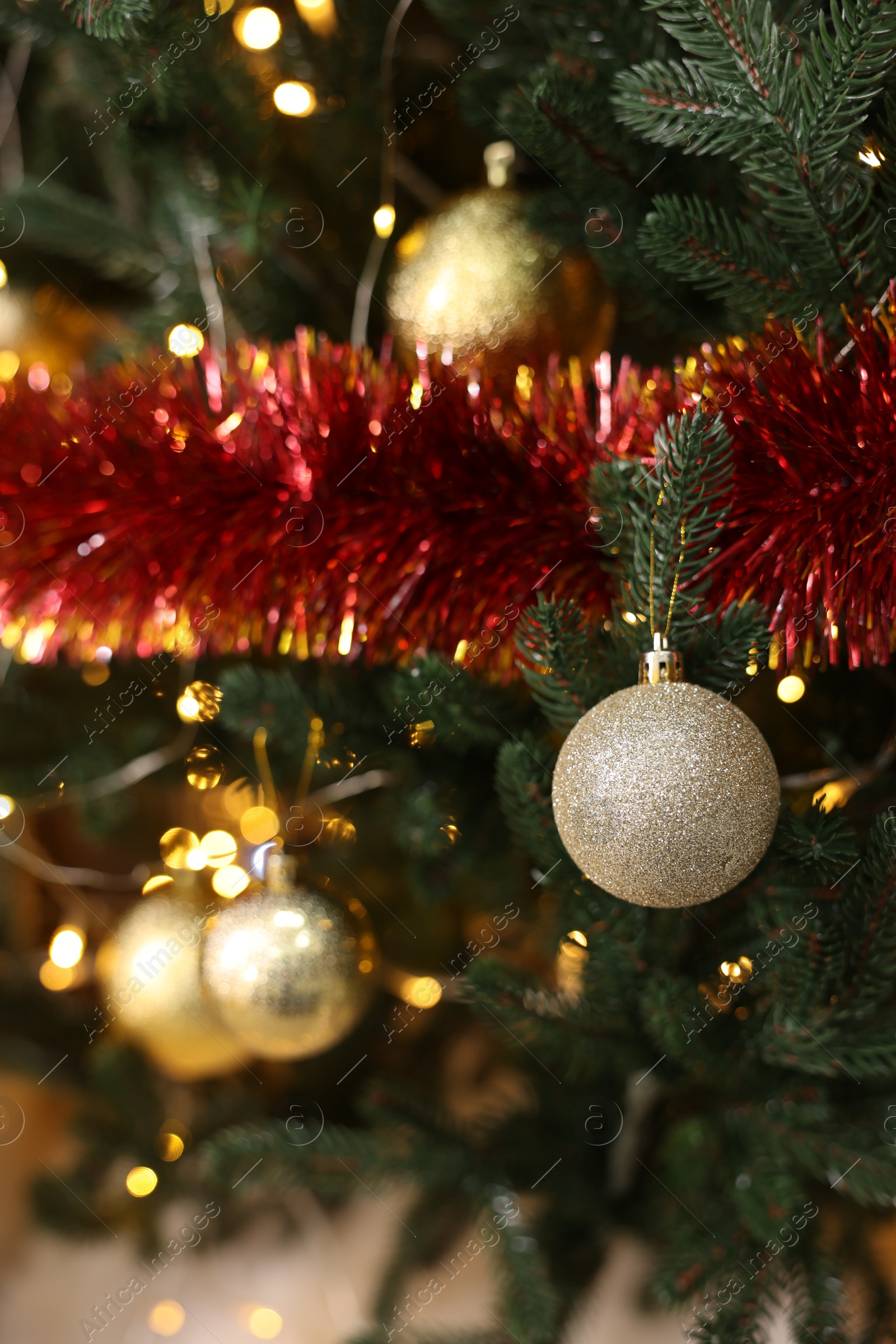 Photo of Shiny tinsel, baubles and festive lights on Christmas tree, closeup