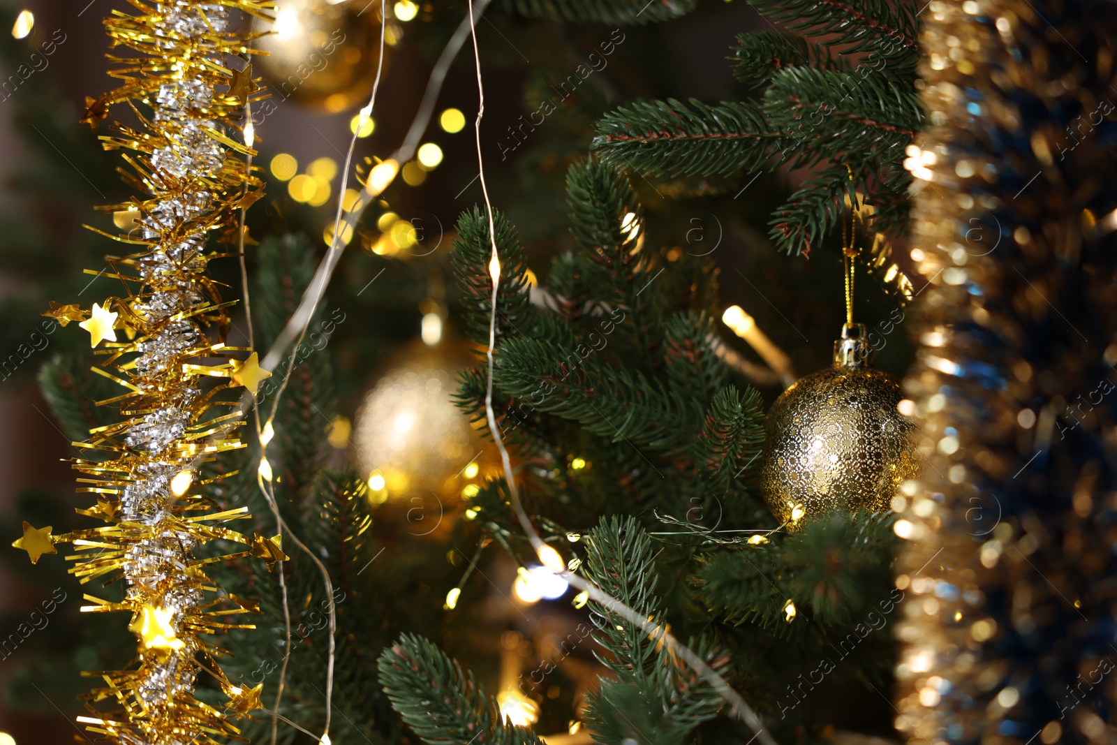 Photo of Shiny tinsels, baubles and festive lights on Christmas tree, closeup