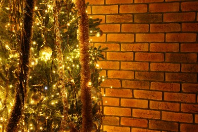 Photo of Shiny tinsels, baubles and festive lights on Christmas tree near brick wall. Space for text