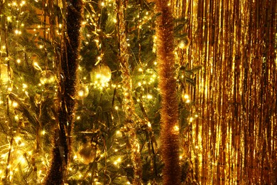 Photo of Shiny tinsels, baubles and festive lights on Christmas tree near foil curtain