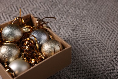 Photo of Shiny tinsels and baubles in cardboard box on carpet, closeup. Space for text