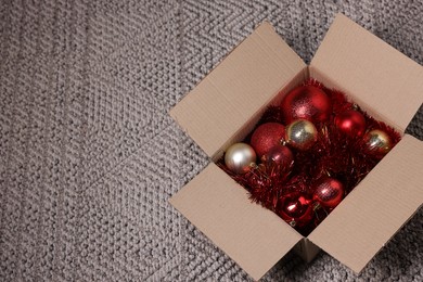 Photo of Shiny tinsels and baubles in cardboard box on carpet, space for text