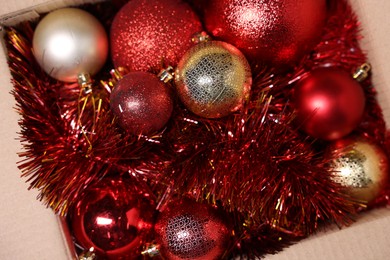 Photo of Shiny tinsels and baubles in cardboard box, top view