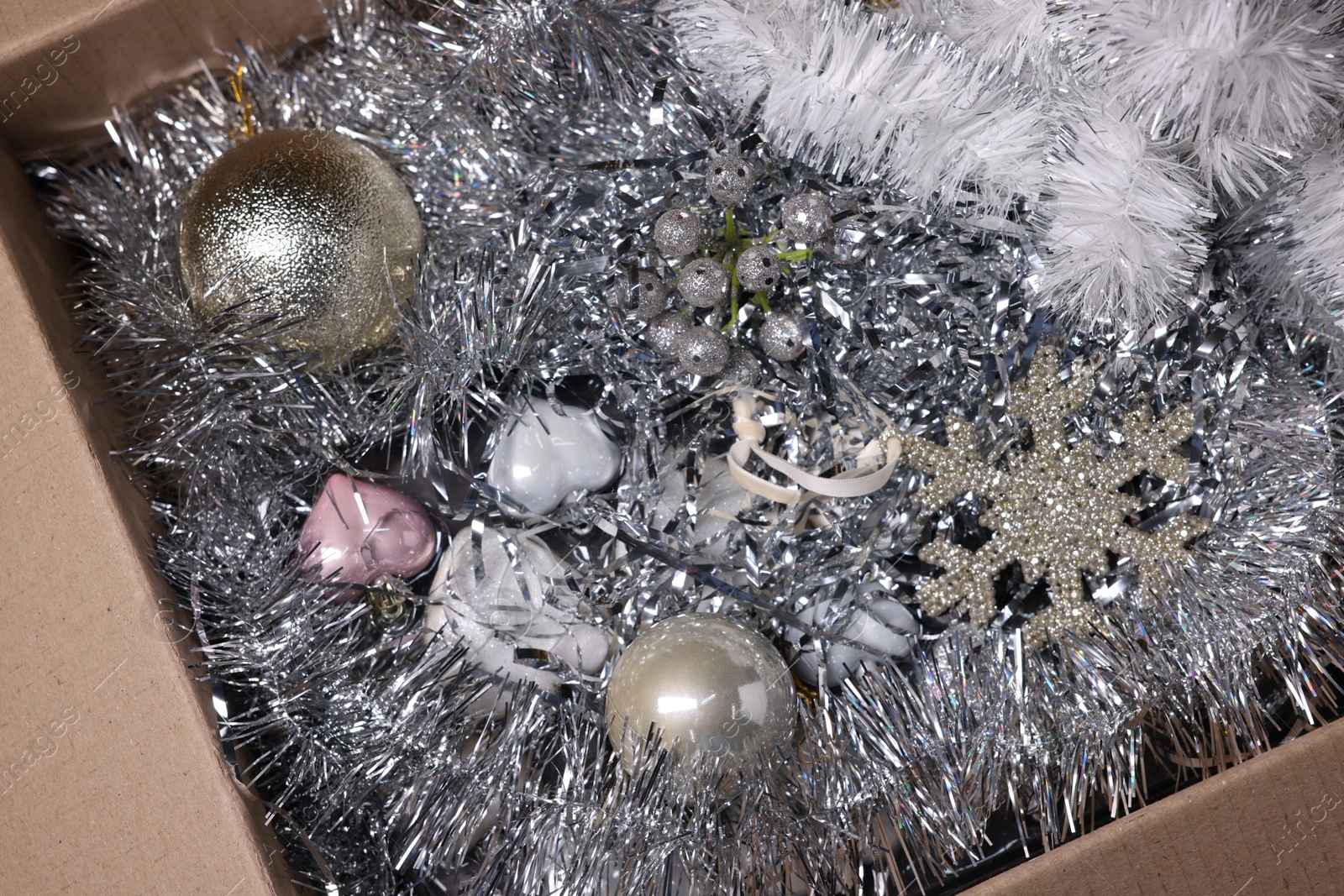 Photo of Shiny tinsels, baubles and other Christmas decor in cardboard box, top view