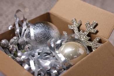 Photo of Shiny tinsels, baubles and other Christmas decor in cardboard box against blurred background, closeup