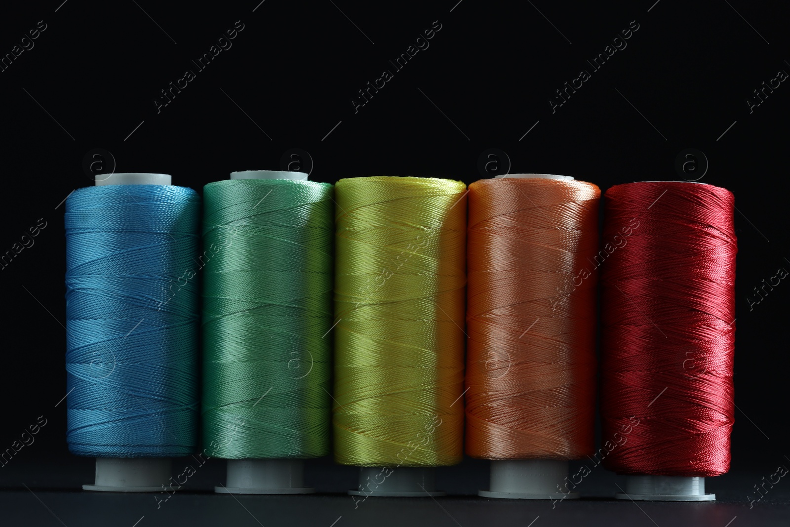 Photo of Spools of colorful sewing threads on black background