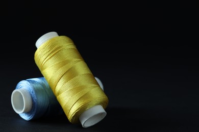 Photo of Spools of colorful sewing threads on black background, closeup. Space for text