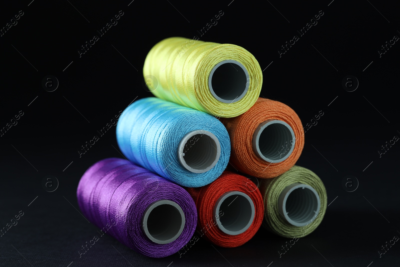 Photo of Spools of colorful sewing threads on black background, closeup