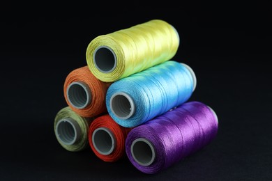 Photo of Spools of colorful sewing threads on black background, closeup