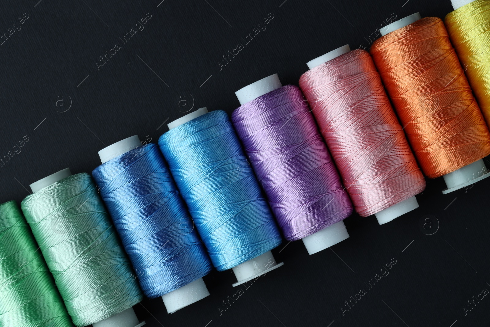 Photo of Spools of colorful sewing threads on black background, flat lay