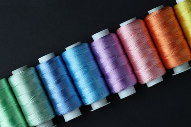 Photo of Spools of colorful sewing threads on black background, flat lay