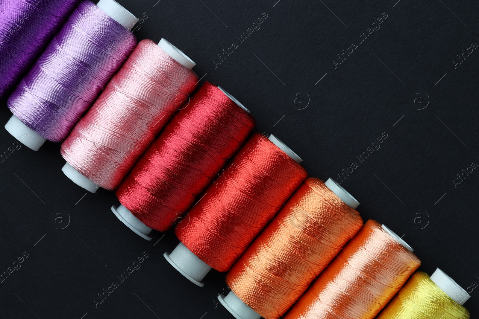 Photo of Spools of colorful sewing threads on black background, flat lay