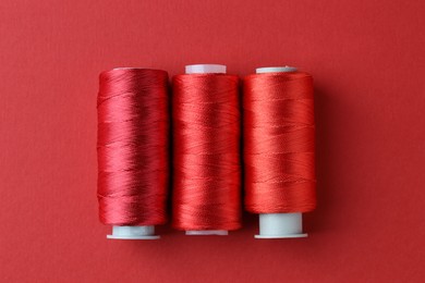 Photo of Spools of colorful sewing threads on red background, flat lay