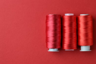 Photo of Spools of colorful sewing threads on red background, flat lay. Space for text