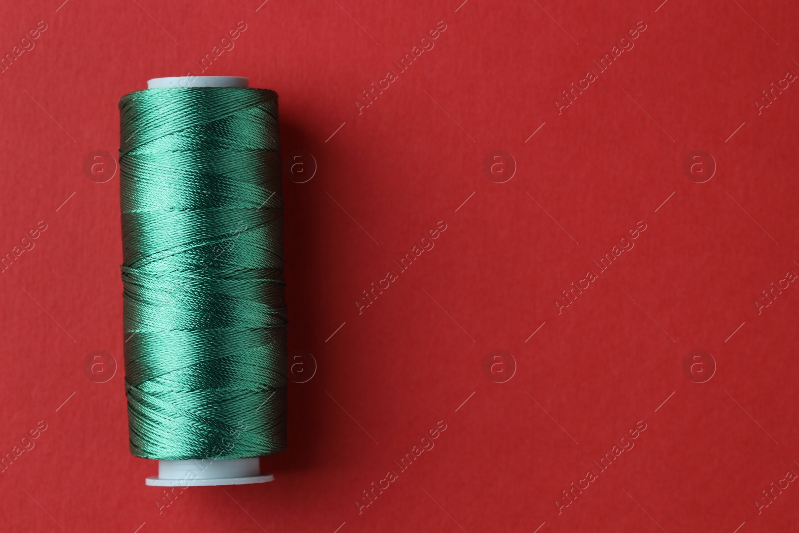 Photo of Spool of green sewing thread on red background, top view. Space for text