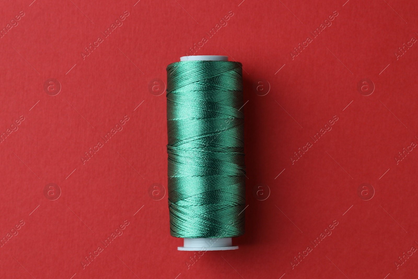 Photo of Spool of green sewing thread on red background, top view