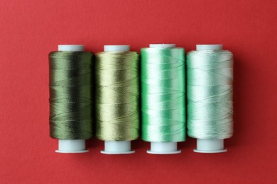 Photo of Spools of colorful sewing threads on red background, flat lay