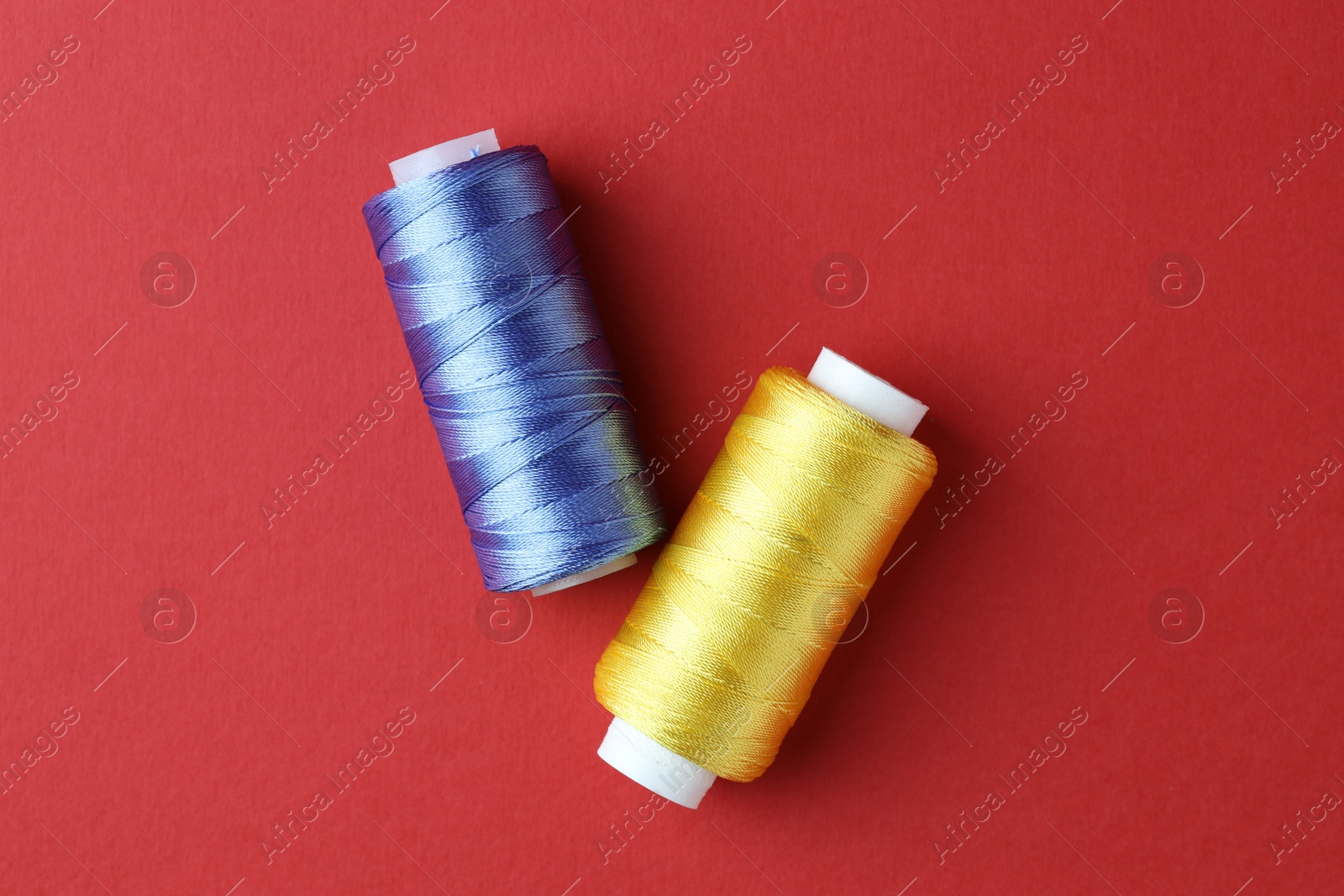 Photo of Spools of colorful sewing threads on red background, flat lay