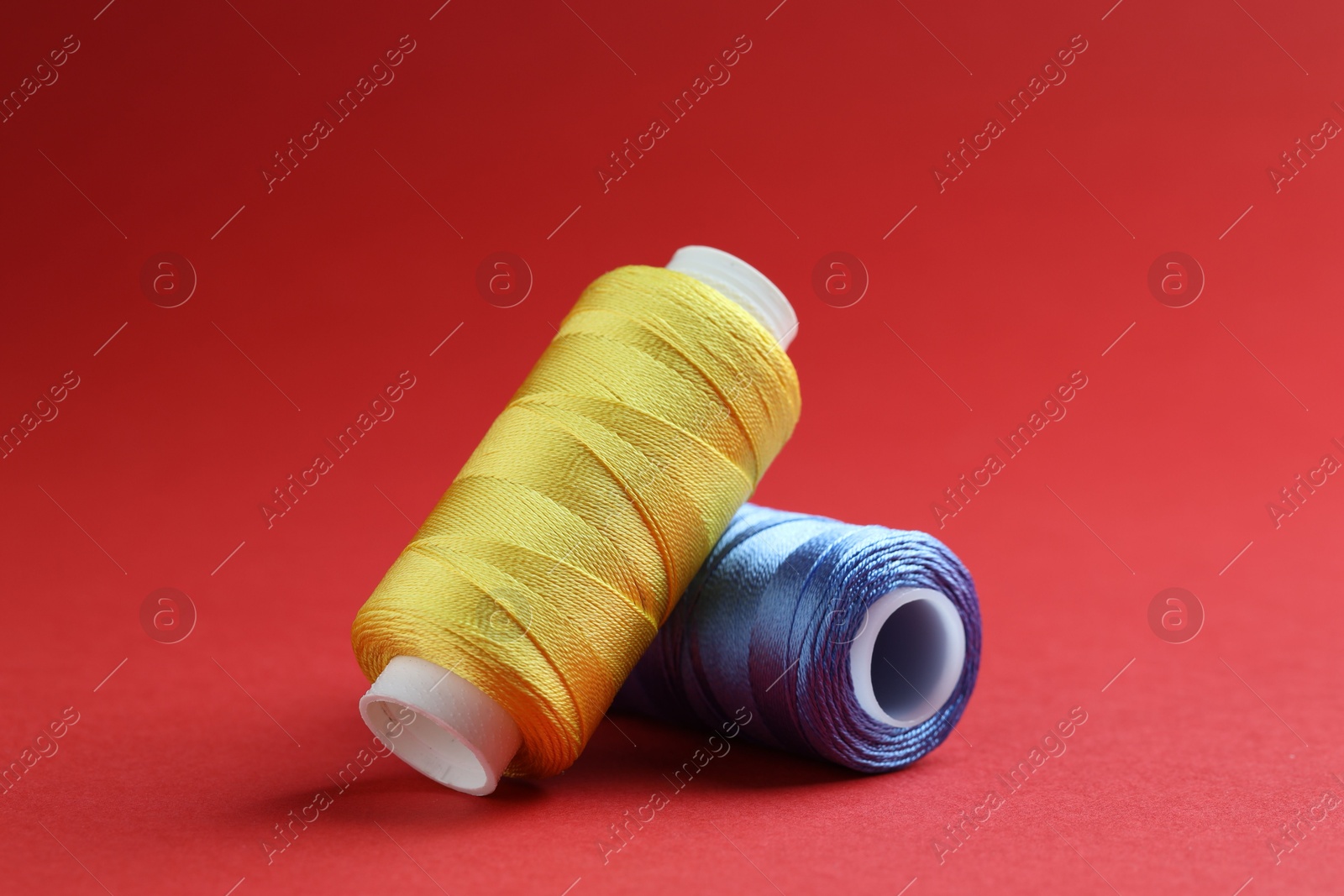 Photo of Spools of colorful sewing threads on red background, closeup