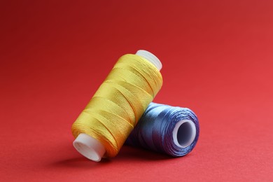 Photo of Spools of colorful sewing threads on red background, closeup